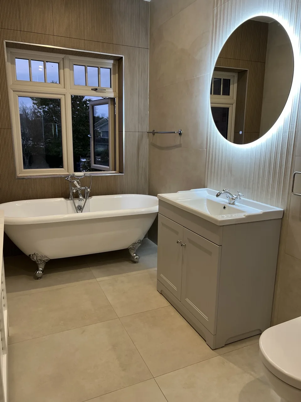 Limerick bathroom with a clawfoot freestanding bath, beige tiles, ribbed wall detail and illuminated oval mirror